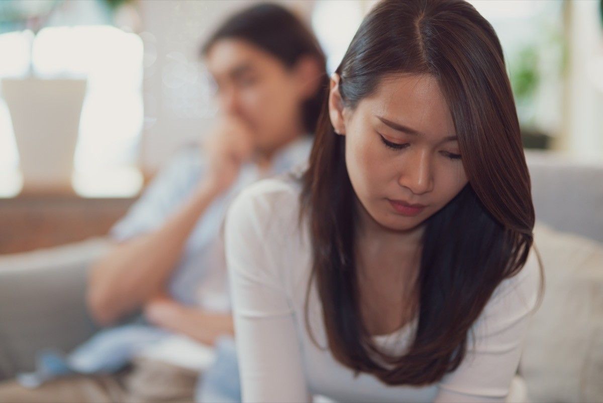 young asian woman looking down with man on bed behind her