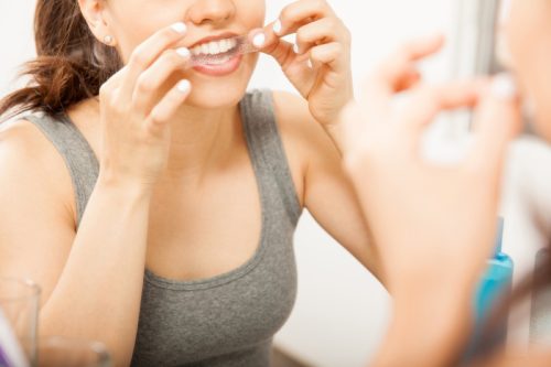 woman using tooth whitening strip, ways you're damaging teeth