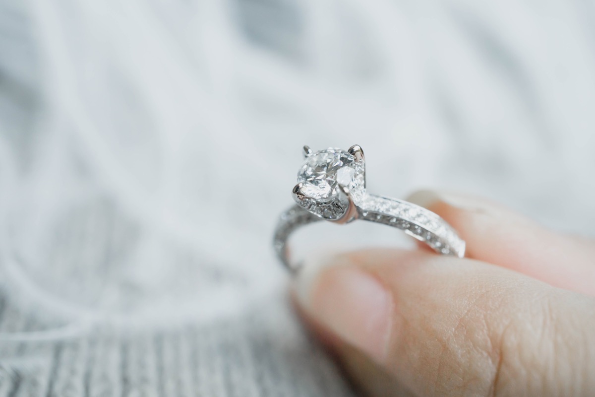 Closeup of woman's fingers holding engagement ring, postpone wedding