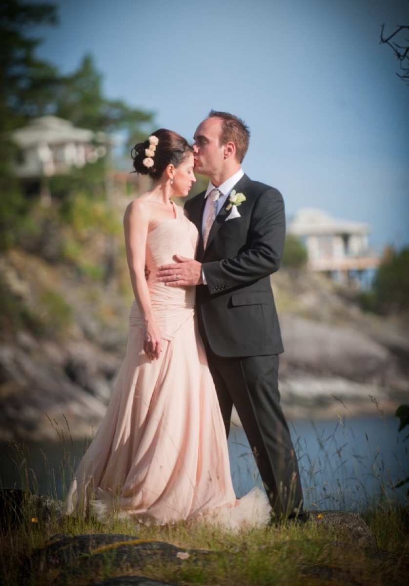 Groom kisses bride on head during wedding ceremony on cliff, postponed wedding