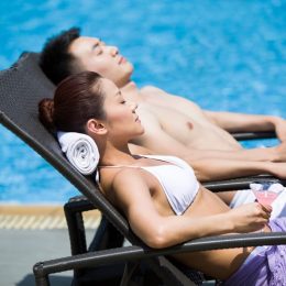 young couple sunbathing in affordable swimsuits by the pool