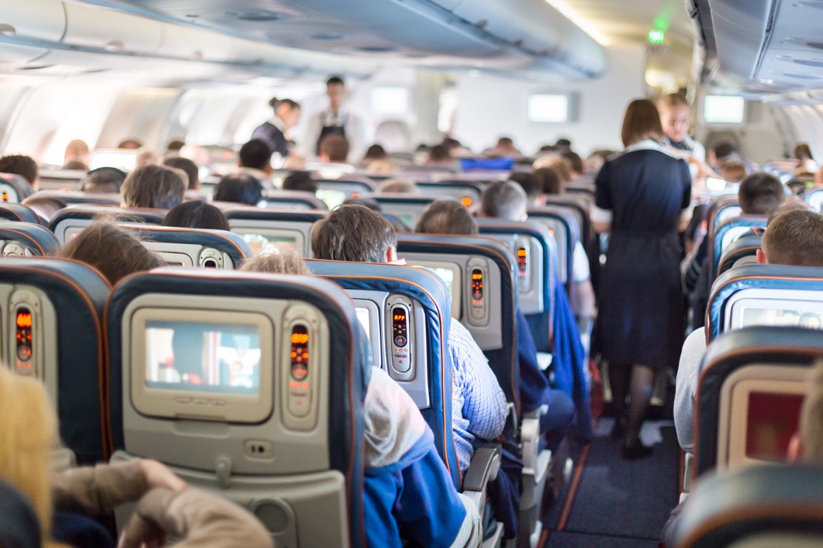a flight attendant walks down the aisle of a crowded airplane