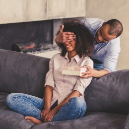man covering woman's eyes and giving her present, best gifts for girlfriend