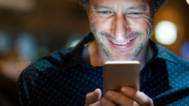 Closeup face of happy mature businessman messaging on cellphone at night on the street with the lights of the road blurred in the background.