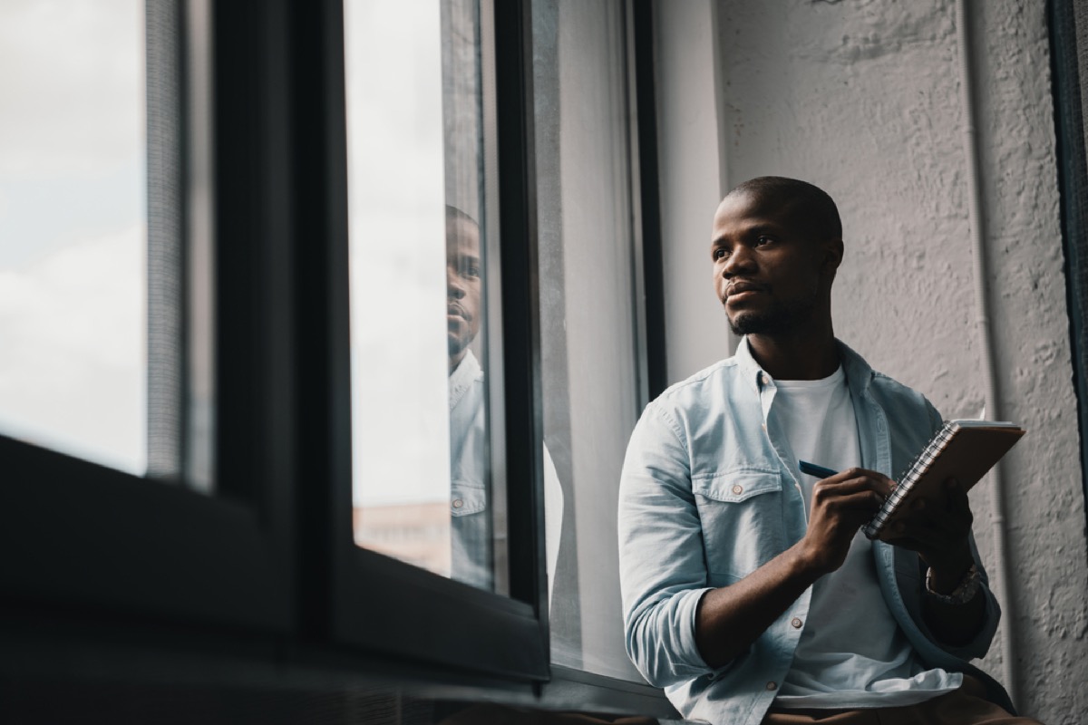 black man sitting by window writing in notebook, smart person habits