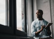 black man sitting by window writing in notebook, smart person habits