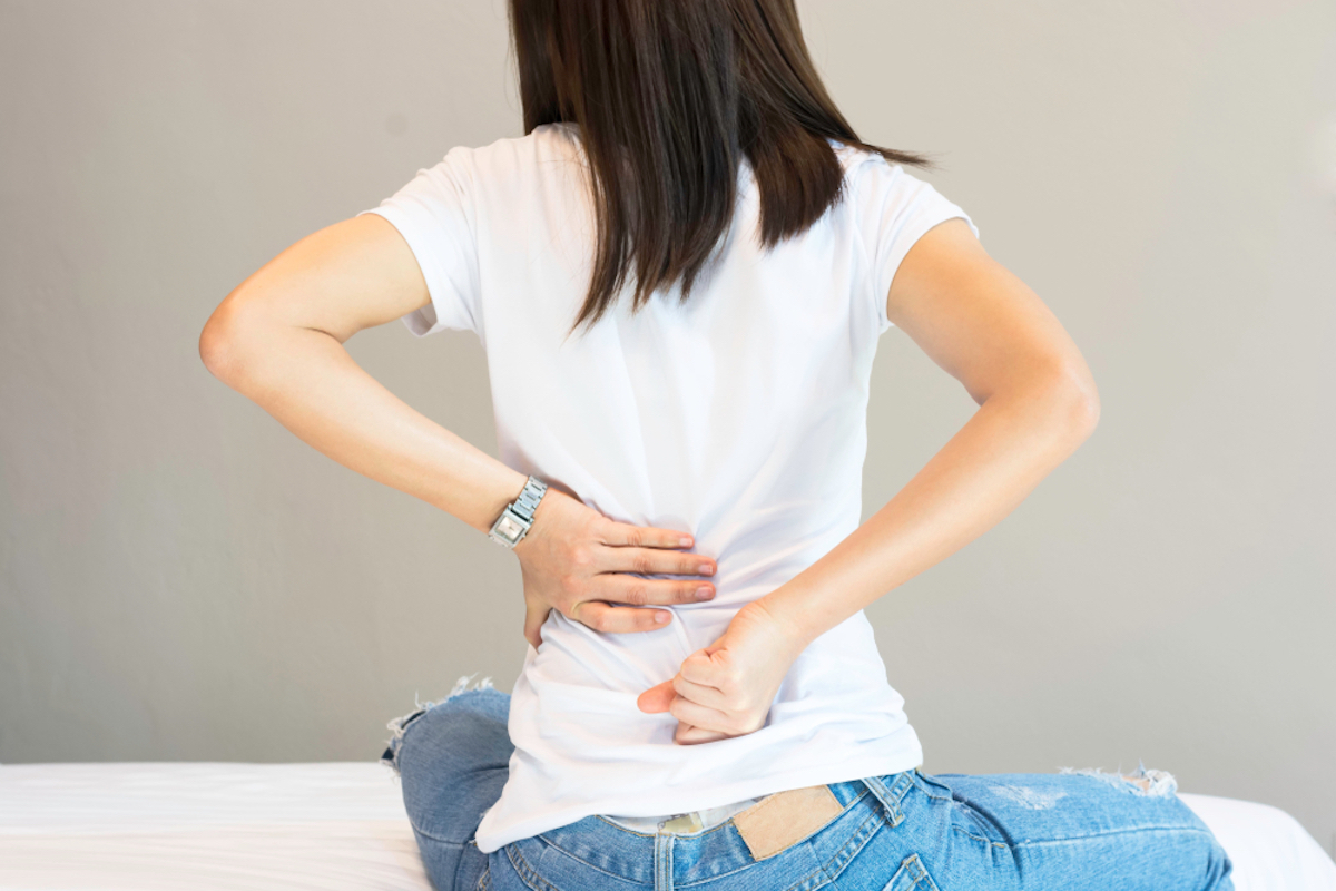 woman in white t-shirt has back facing to camera and is massaging lower back