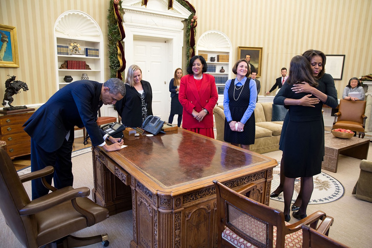 DT2WNM US President Barack Obama signs items at the Resolute Desk after he and First Lady Michelle Obama met with mothers regarding the Affordable Care Act, in the Oval Office of the White House December 18, 2013 in Washington, DC.