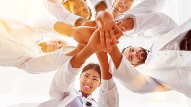 a bunch of doctors smiling and putting their hands together in a circle showing team spirit