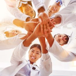 a bunch of doctors smiling and putting their hands together in a circle showing team spirit