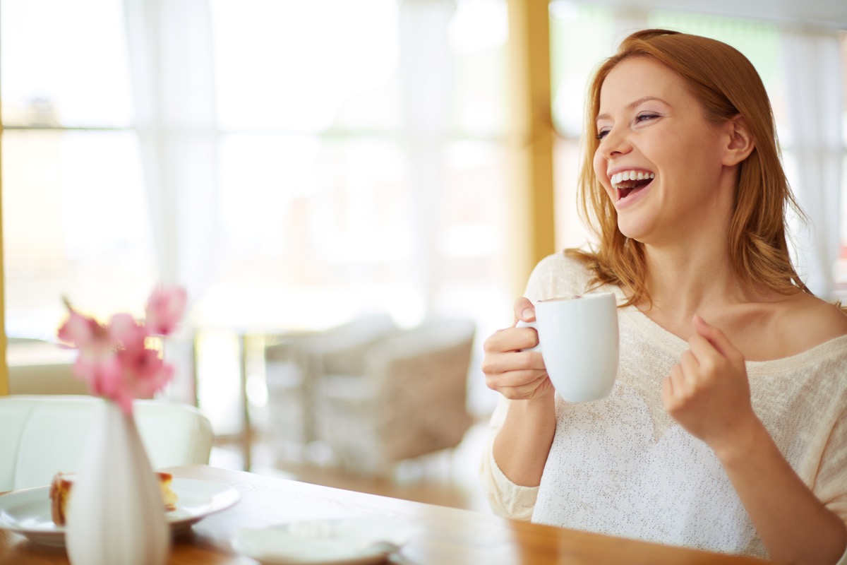 Red-haired woman smiling and drinking coffee