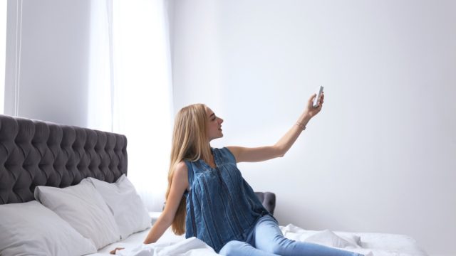 woman turning on air conditioning from bed