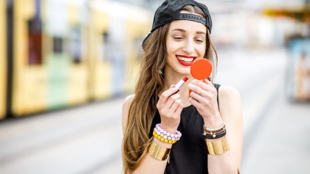 hipster woman applying red lipstick outdoors, summer beauty products