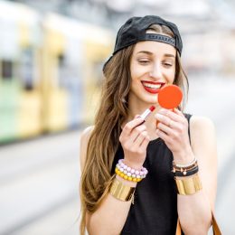 hipster woman applying red lipstick outdoors, summer beauty products