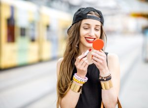 hipster woman applying red lipstick outdoors, summer beauty products