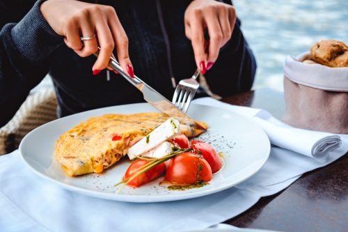 A woman eating scrambled eggs, cheese, tomatoes and bread at a waterside restaurant