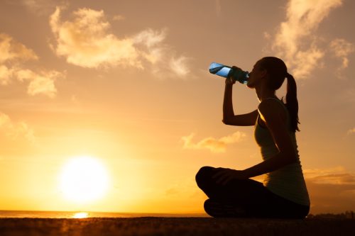 woman outdoors drinking water in front of sunset, cute water bottles