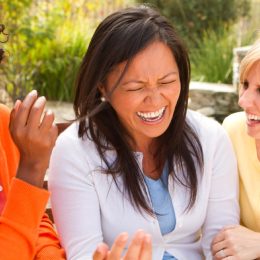 three middle-aged women laughing outdoors, female friend