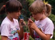 In 1980s, Two young twin sisters sip Coke from their own curly straws in an English garden, UK