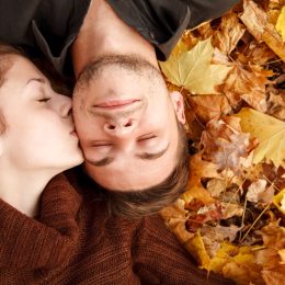 woman kissing man on the cheek while laying down in the foliage - romantic fall date ideas