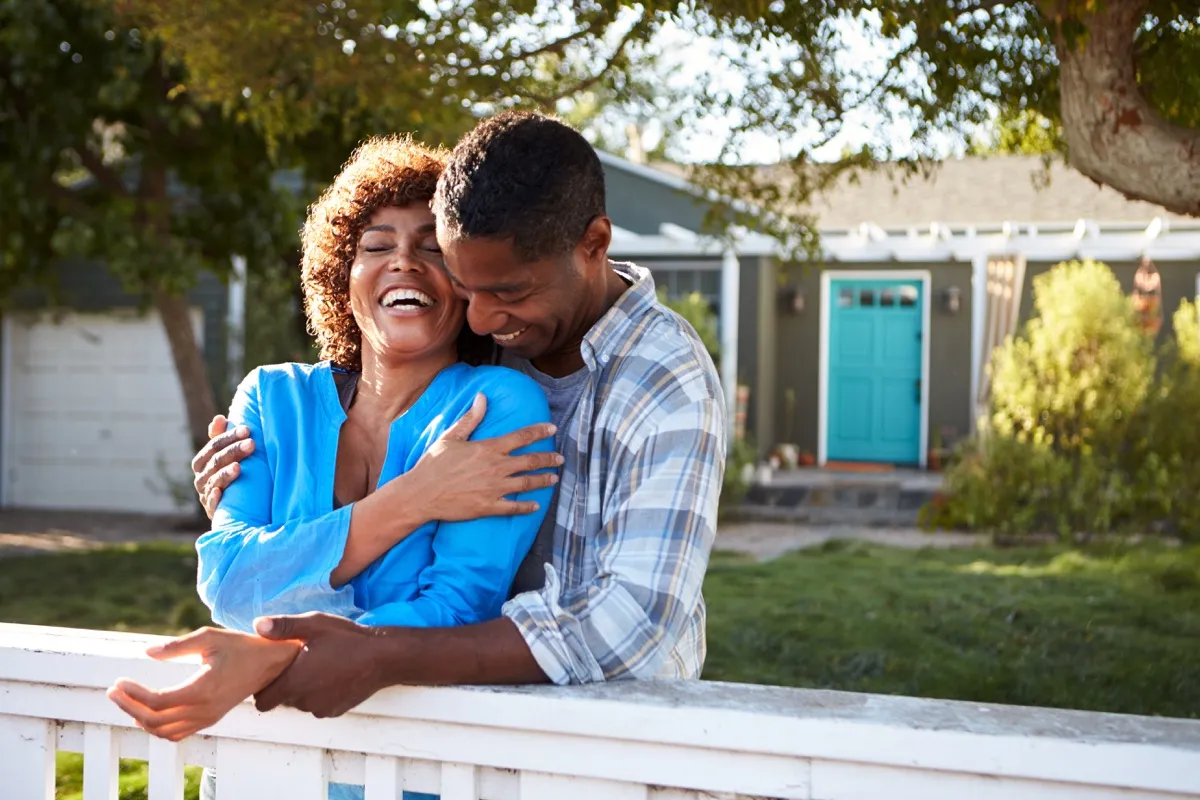 older black couple smiling and laughing outside while leaning on fence