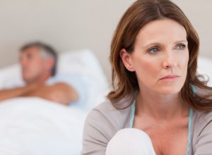 white woman sitting at the end of the bed while white older man sleeps