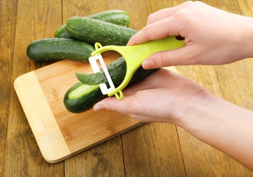white hand peeling cucumber over wooden cutting board
