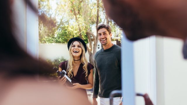 couple arriving at party with bottle of wine, housewarming gifts