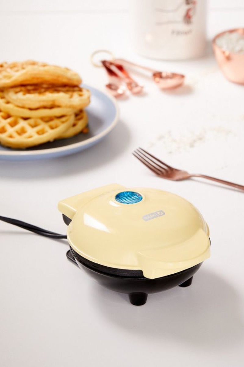 yellow waffle maker on white countertop with plate of waffles behind it