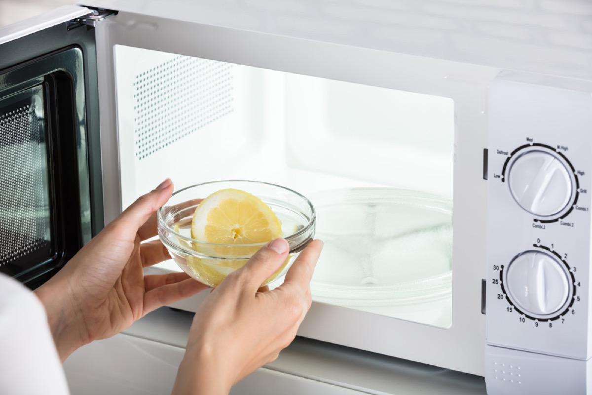 woman placing lemon in bowl into microwave, old school cleaning tips