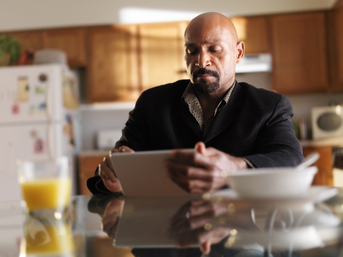 man sitting in kitchen playing on ipad in front of a glass of orange juice