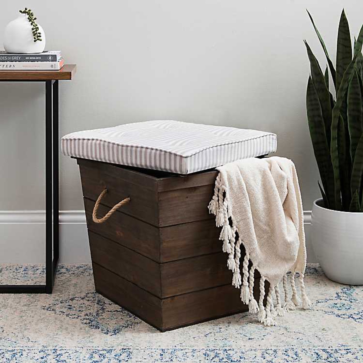 brown ottoman with white top and white blanket with tassels hanging over the side