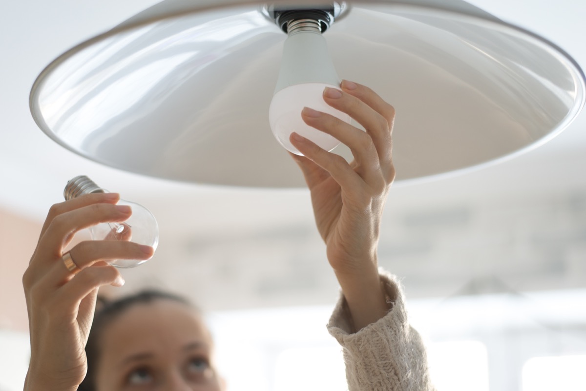 woman installing white lightbulb in home, fire prevention tips