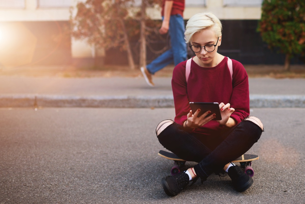 young woman sitting on a skateboard holding an ipad