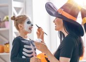 Mother dressed as witch painting skeleton makeup on little girl