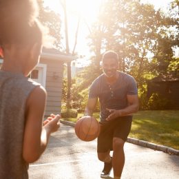 father and child playing basketball in suburbia