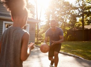 father and child playing basketball in suburbia