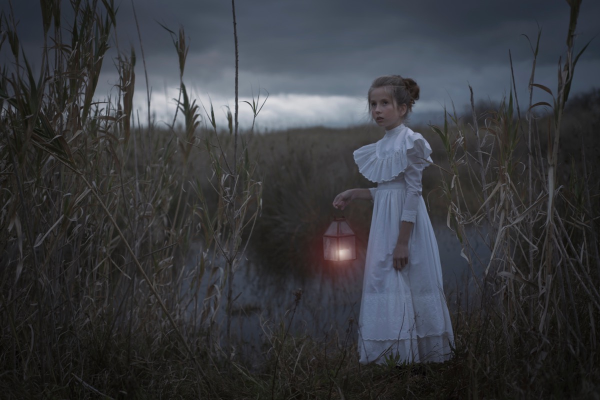 girl in dark forest holding a lantern