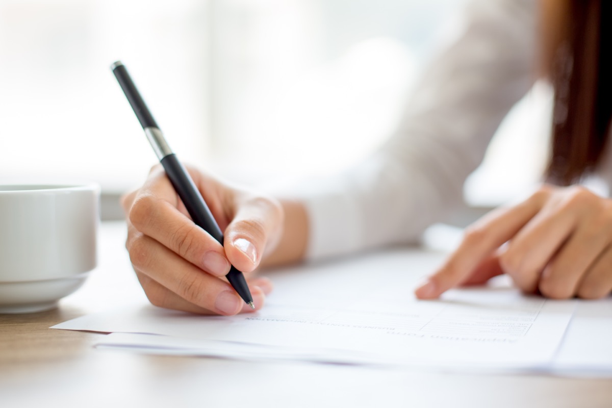 Woman using a pen to write at her desk office germs