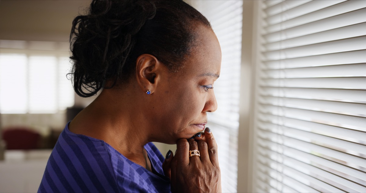 older black woman looking out window looking sad