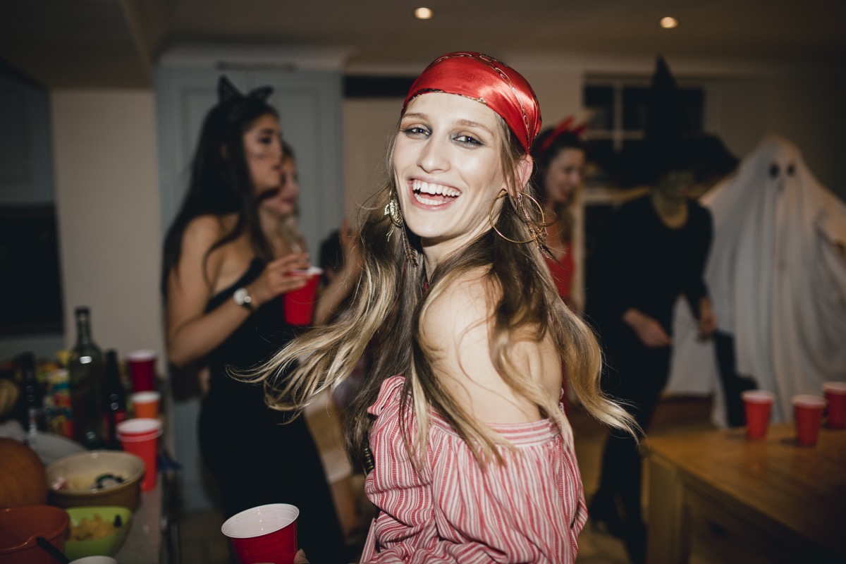 Woman dressed as a pirate at a Halloween party laughing and dancing as she looks back towards the camera.