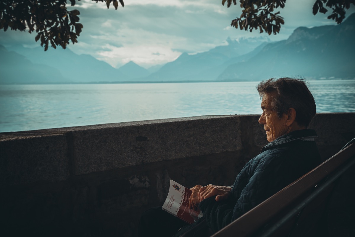 Older man sitting outside reading a book in another language