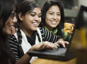 Indoor image of a group of late teen girls from different ethnicities using laptop together
