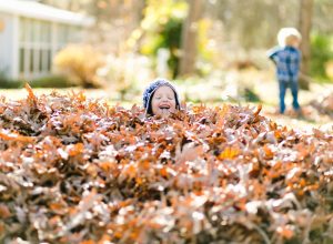 toddler jumping in pile of leaves in fall