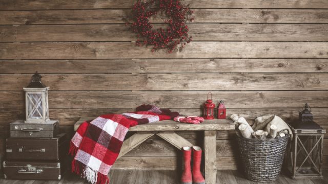 wooden wall with wreath and bench with blanket draped over it and red boots, rustic farmhouse decor