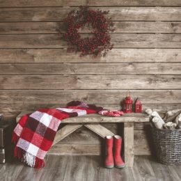 wooden wall with wreath and bench with blanket draped over it and red boots, rustic farmhouse decor