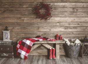 wooden wall with wreath and bench with blanket draped over it and red boots, rustic farmhouse decor