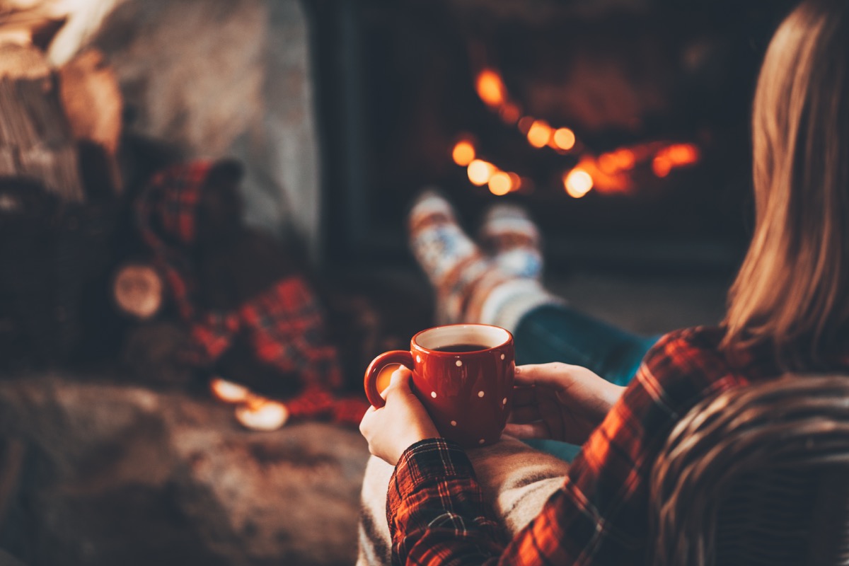 woman drinking tea or coffe by a fire in fall or winter