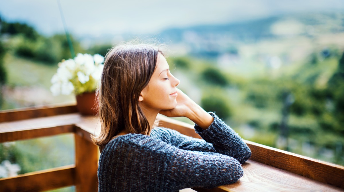 woman smiling with her eyes closed outside smelling fresh air