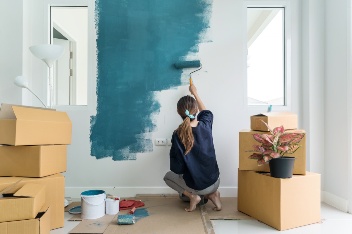 young white woman in empty home painting wall green